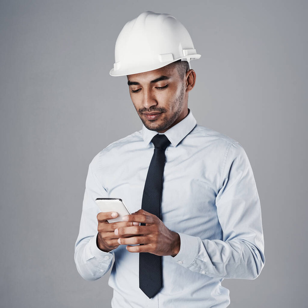 Даю добро его команде. хорошо одетый инженер-строитель, использующий свой мобильный телефон, стоя в студии - Фото, изображение
