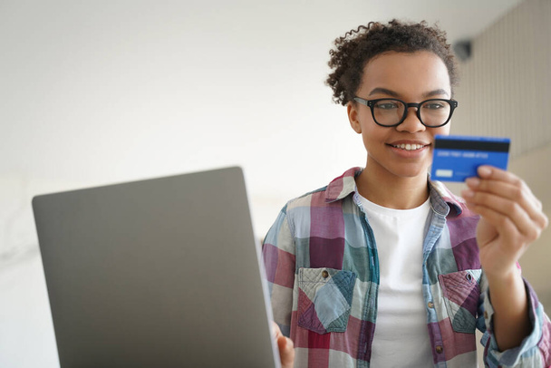 Mieszana nastolatka rasy zarządza swoimi finansami, pewnie posiadając kartę kredytową i korzystając z usług bankowości internetowej na swoim laptopie do celów e-commerce w domu. - Zdjęcie, obraz