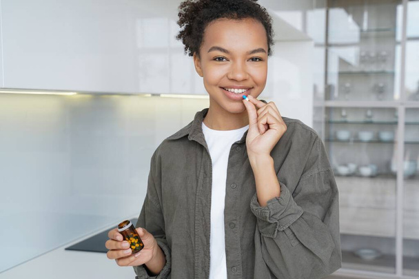 Menina birracial radiante sorri como ela toma suplementos dietéticos, vitaminas, garantindo a pele saudável e cabelo para uma aparência confiante. - Foto, Imagem