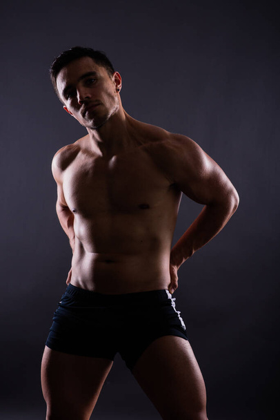 Μυώδη shirtless νεαρός άνδρας στέκεται αυτοπεποίθηση, μπροστά άποψη, κοιτάζοντας μια φωτογραφική μηχανή - Φωτογραφία, εικόνα