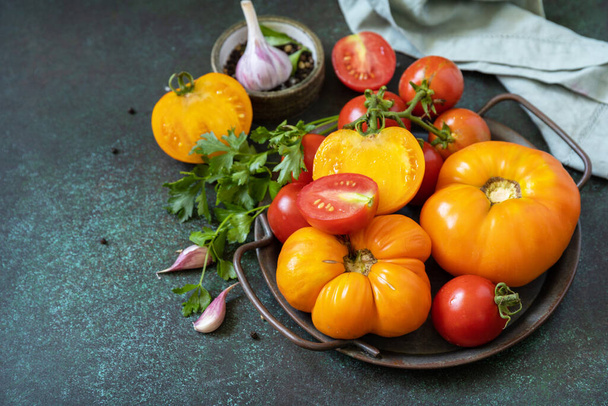 Verschiedene bunte Tomaten und Petersilienblätter auf dunklem Steingrund. Bio-Lebensmittel. Kopierraum.  - Foto, Bild