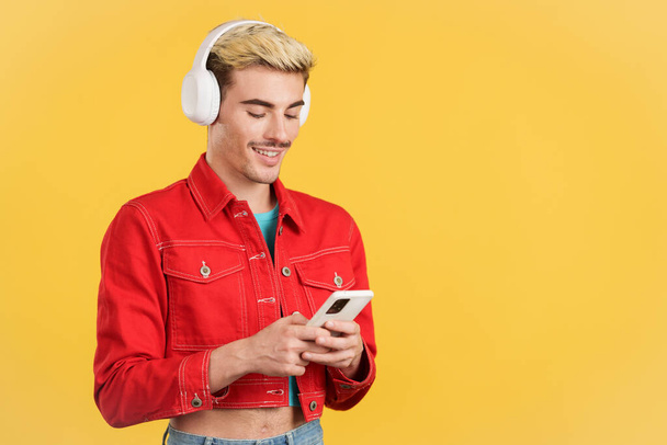 Gay άνθρωπος ακούγοντας μουσική με ακουστικά και ένα κινητό στο στούντιο με κίτρινο φόντο - Φωτογραφία, εικόνα