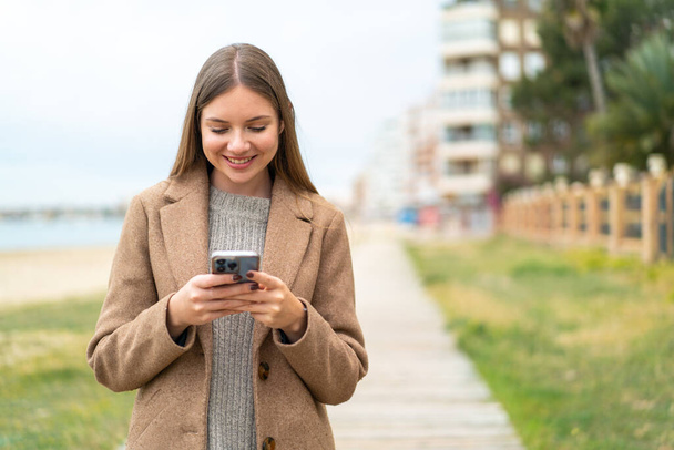 Jovem mulher loira bonita enviando uma mensagem ou e-mail com o celular - Foto, Imagem