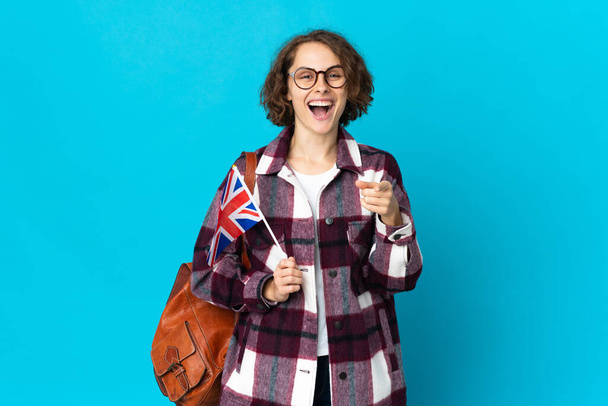 Junge Engländerin mit britischer Flagge auf blauem Hintergrund überrascht und zeigt nach vorne - Foto, Bild