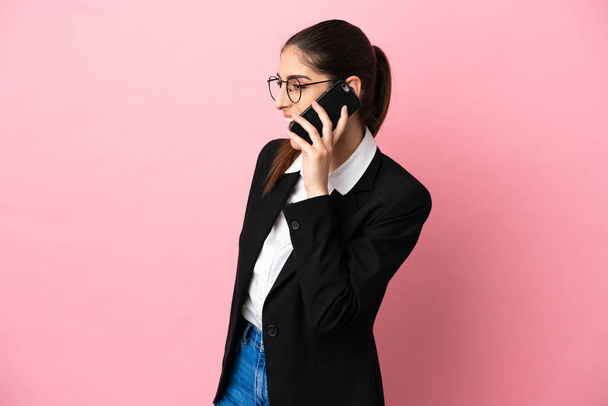 Junge kaukasische Geschäftsfrau isoliert auf rosa Hintergrund hält ein Gespräch mit dem Handy mit jemandem - Foto, Bild