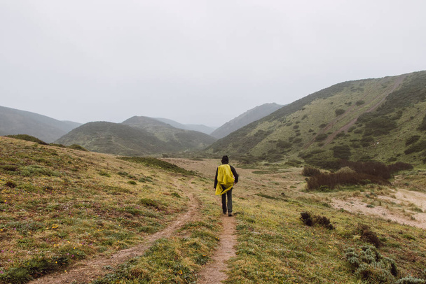 Wandering in heavy rain and wearing a raincoat along the Fisherman Trail in the southern part of Portugal during rainy weather heading to Cape St. Vicente. Rough landscape. - Valokuva, kuva