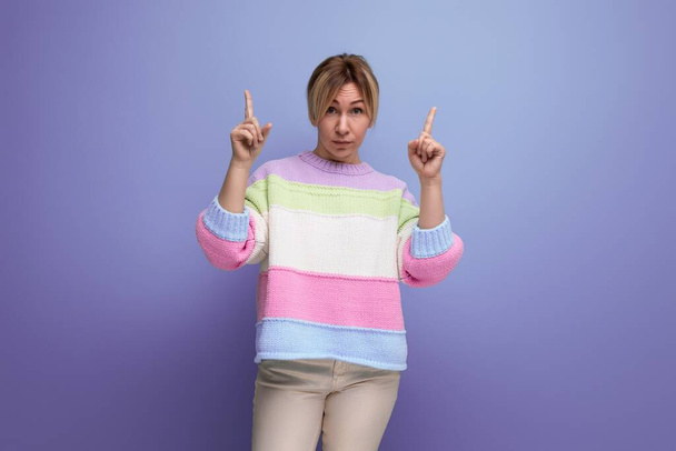 blond young woman demonstrates with her hands on the free space of the wall on a purple background. - Foto, Imagen
