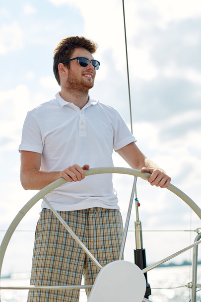 young man in sunglasses steering wheel on yacht - Foto, afbeelding