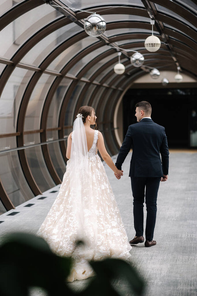 Back view of groom and bride walk in the big hall with windows. Elegant bride and groom. High quality photo - Φωτογραφία, εικόνα