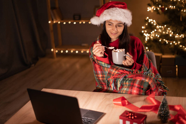 Молодая красивая женщина смотрит кино и ест зефир, сидя дома, завернутый в уютную теплую клетчатую клетку в канун Рождества. Копирование пространства - Фото, изображение