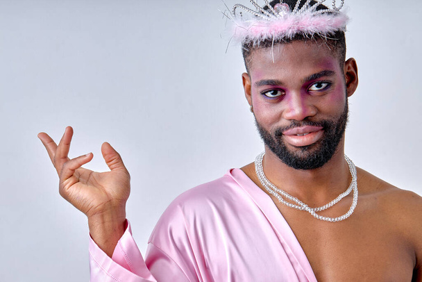 Awesome black half-naked man in crown posing at camera like a fairy, princess. young guy of black american appearance with dark skin and beard, bright party make-up, alone. beauty, lgbtq - Photo, image