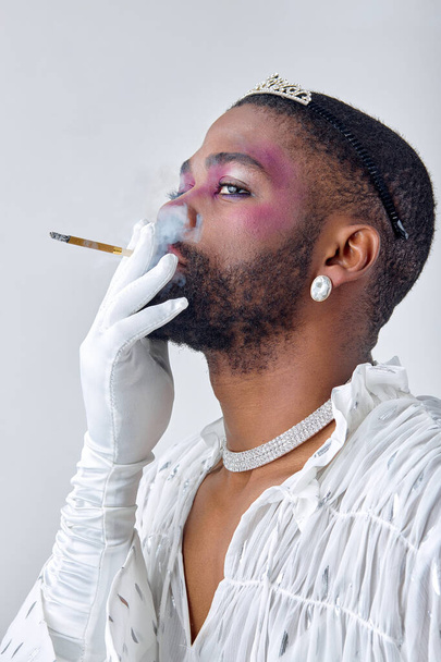 Young beautiful black american gay man with make up in stylish shirt smoking cigarette, looking at side isolated on white background studio portrait People lgbt lifestyle, fashion concept - Фото, зображення