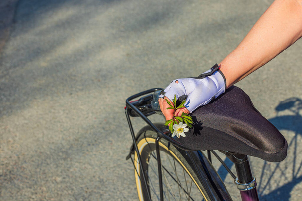 Beautiful view of woman's hand in sports gloves holding with white flower on bicycle seat. Sweden. - Photo, Image