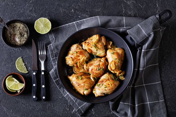 garlic rosemary thyme herbed fried chicken thighs on skillet on concrete table with cutlery, horizontal view from above, flat lay - Fotoğraf, Görsel