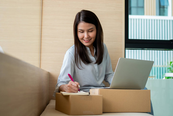 Glückliche junge asiatische Unternehmerin, Lächeln für den Verkaufserfolg nach Überprüfung der Bestellung im Online-Shopping-Geschäft in einem Laptop im Home Office, Konzept des Kaufmannsgeschäfts online und E-Commerce - Foto, Bild