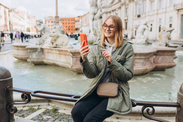 Muotokuva iloinen onnellinen nainen taustalla Piazza Navona Roomassa, Italiassa. Kaunis hymyilevä naaras takissa älypuhelimella ulkona. Kaupunkien elämäntavan käsite. - Valokuva, kuva