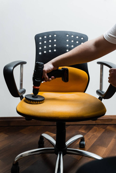 Smearing detergent on armchair using drill with brush for dry cleaning. Applying detergent on chair in home interior for dry cleaning - Foto, immagini