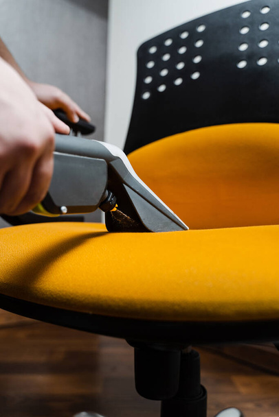 El ama de llaves está extrayendo suciedad del sillón amarillo utilizando una máquina de extracción de limpieza en seco. El limpiador es una silla de limpieza con máquina extractora de aspiradora de lavado para muebles tapizados limpios en seco - Foto, Imagen