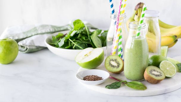 Un batido verde saludable en una botella rodeada de ingredientes frescos para hacerlo.  - Foto, imagen