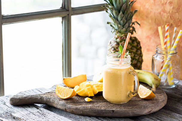 Een verfrissende mango citrus smoothie op een rustieke plank tegen een raam, klaar om te drinken. - Foto, afbeelding