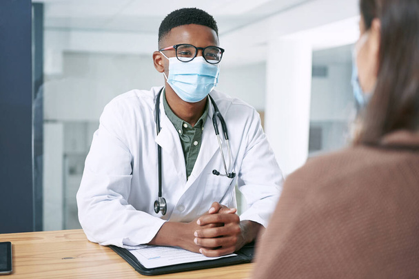 Axé sur la santé et de bonnes relations. un jeune médecin assis avec son patient et portant son masque facial lors d'une consultation à la clinique - Photo, image