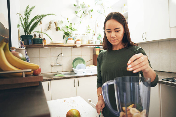 Entre no maior número possível de ingredientes. uma jovem mulher preparando um smoothie em casa - Foto, Imagem