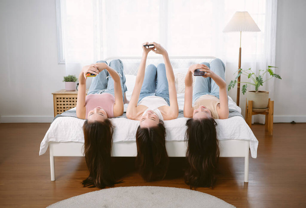 Trzy młode Azjatki urocze, urocze, urocze, atrakcyjne, wesołe, szczęśliwe twarze leżące na łóżku i piszące za pomocą smartfona. Koreańskie dziewczyny to media społecznościowe i rozmowy. Styl życia, Koncepcja przyjaźni - Zdjęcie, obraz