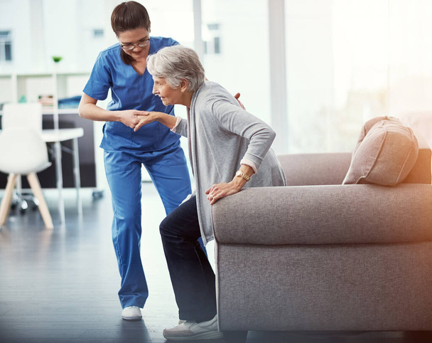 Ahí lo tienes. Foto completa de una joven enfermera ayudando a su paciente mayor a levantarse de una silla en el hogar de ancianos - Foto, imagen