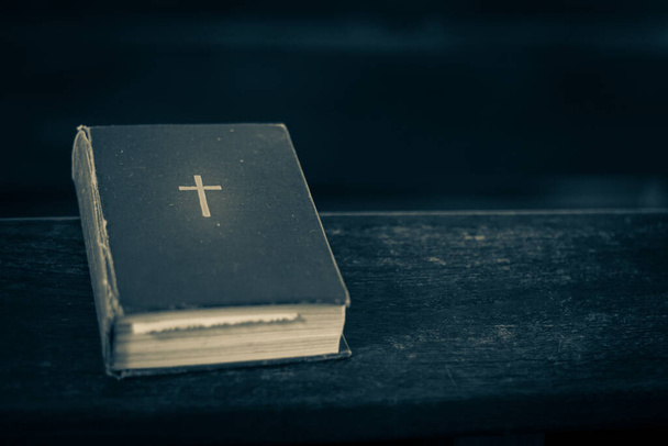 La Biblia en el banco de la iglesia. La palabra de Dios en un pequeño libro. Enfoque selectivo suave. Grano creado artificialmente para la imagen - Foto, Imagen