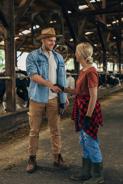 A man with a leghorn shakes hands with a woman working in a stable. - Foto, Bild