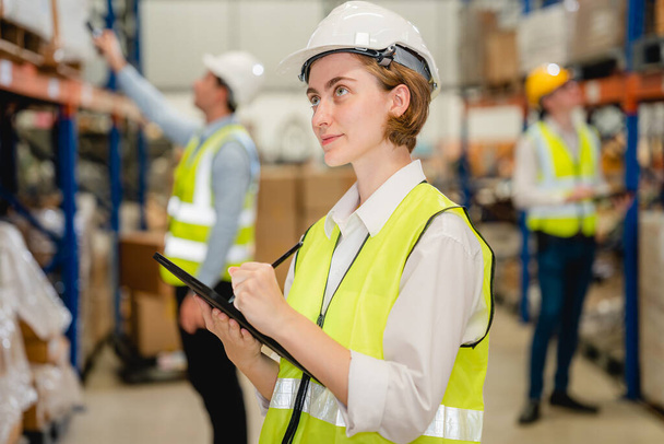 Happy warehouse engineer with safety vest using tablet checking goods and supplies on shelves with goods background in warehouse store, Logistic and business export concept - Fotó, kép