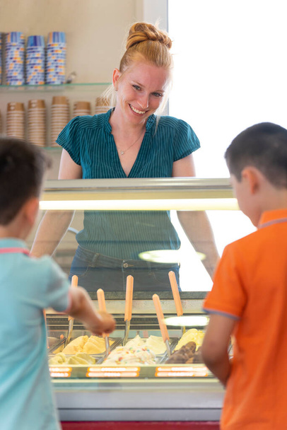 Γυναίκα που σερβίρει παγωτό σε δύο παιδιά σε παγωτατζίδικο - Φωτογραφία, εικόνα