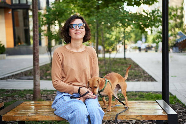 Giovane donna adulta in città con un cane seduto e abbracciato, sorridente. Accarezzare il cane, nutrirsi, divertirsi Foto di alta qualità - Foto, immagini