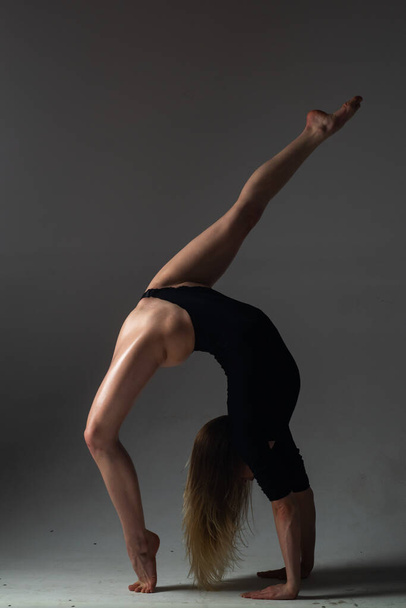 Leg-split. Flexible girl does gymnastic exercises stretching. Beautiful sexy flexible woman demonstrates sexy flexible body. Flexibility stretching on black background. Strong flexible female body - Photo, image