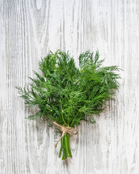 Fresh dill herbs in a bunch. Aromatic healthy spices on a light wooden background. Top view. - Foto, imagen