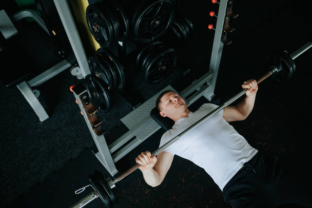 Un jeune homme déterminé à effectuer une séance d'entraînement intense avec un haltère dans la salle de gym, en se concentrant sur sa force physique et l'endurance. Force déchaînée homme s'exerçant avec Barbell dans la salle de gym - Photo, image