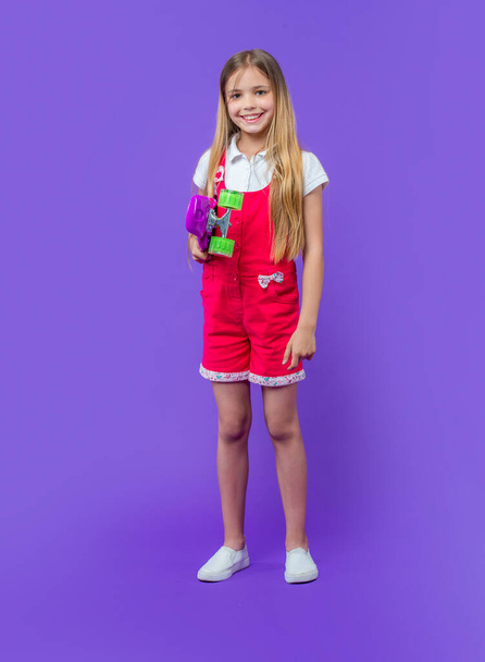 happy teen girl skateboarder isolated on purple. teen girl skateboarder in studio. teen girl skateboarder on background. photo of teen girl skateboarder. - Φωτογραφία, εικόνα