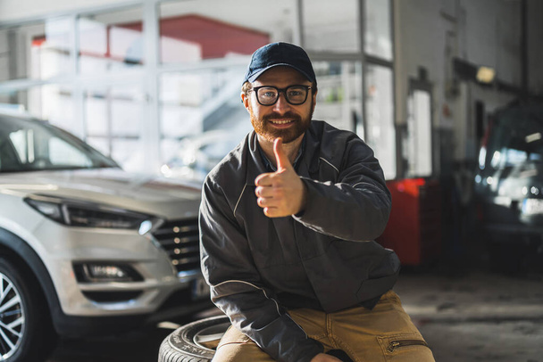 Hombre feliz mecánico de coches mostrando un pulgar hacia arriba, taller de servicio de reparación. Foto de alta calidad - Foto, imagen