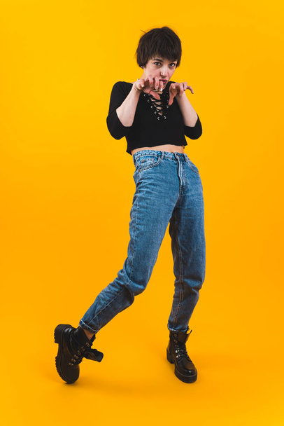 Vollbild einer jungen Frau, die ein schwarzes Oberteil und eine Jeanshose trägt und mit den Händen in einer Krallen-Geste posiert. Vertikaler Schuss. Hochwertiges Foto - Foto, Bild