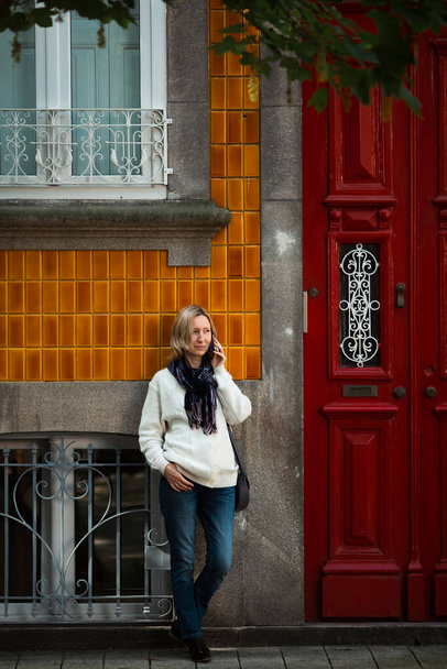 Geleneksel Portekiz şehir evinin girişinde cep telefonuyla konuşan bir kadın var..  - Fotoğraf, Görsel