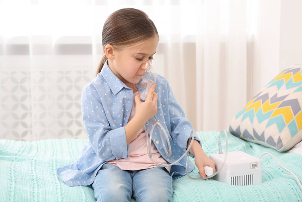 Sick little girl using nebulizer for inhalation on bed at home - Foto, imagen