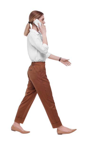 Beautiful businesswoman talking on smartphone while walking against white background - Foto, afbeelding