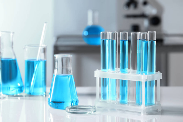 Test tubes with light blue liquid and different laboratory glassware on table - Foto, Imagen