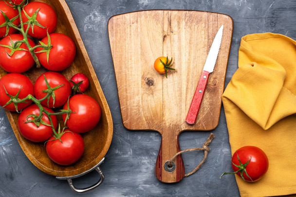 bunch of fresh, ripe tomatoes in wooden dish and  cutting board with  knife on gray background. View from above. Space for text. - Φωτογραφία, εικόνα