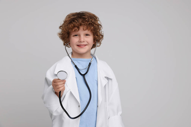 Маленький мальчик в медицинской форме со стетоскопом на светло-сером фоне. Пространство для текста - Фото, изображение