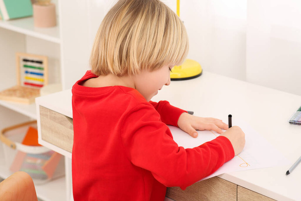 Cute little boy drawing with marker at desk in room, closeup. Home workplace - Fotó, kép