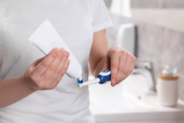 Žena mačkání zubní pasta z trubice na elektrický kartáček v koupelně, detailní - Fotografie, Obrázek