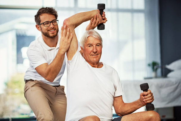Ты должен быть в форме с возрастом. Обрезанный портрет пожилого человека, работающего над своим выздоровлением с мужчиной-физиотерапевтом - Фото, изображение