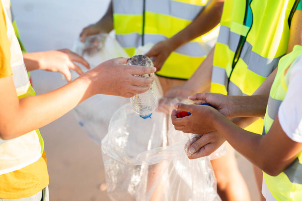 Les adolescents internationaux en uniforme mettent les ordures et les bouteilles en plastique dans le sac pour le recyclage sur la plage, ferment. Environnement soins, nettoyer la planète, protéger la mer, cultivé - Photo, image