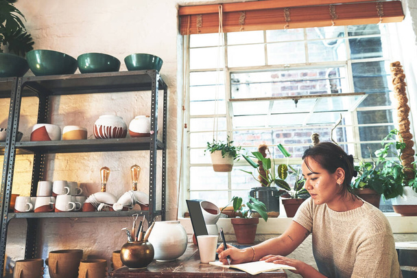 I wouldnt be here today if it wasnt for notes. an attractive young business owner sitting alone in her pottery studio and making notes - 写真・画像